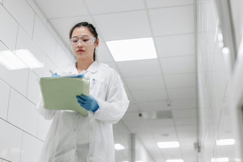 A focused female scientist in a lab coat writes notes in a laboratory hallway, showcasing professionalism in research settings.